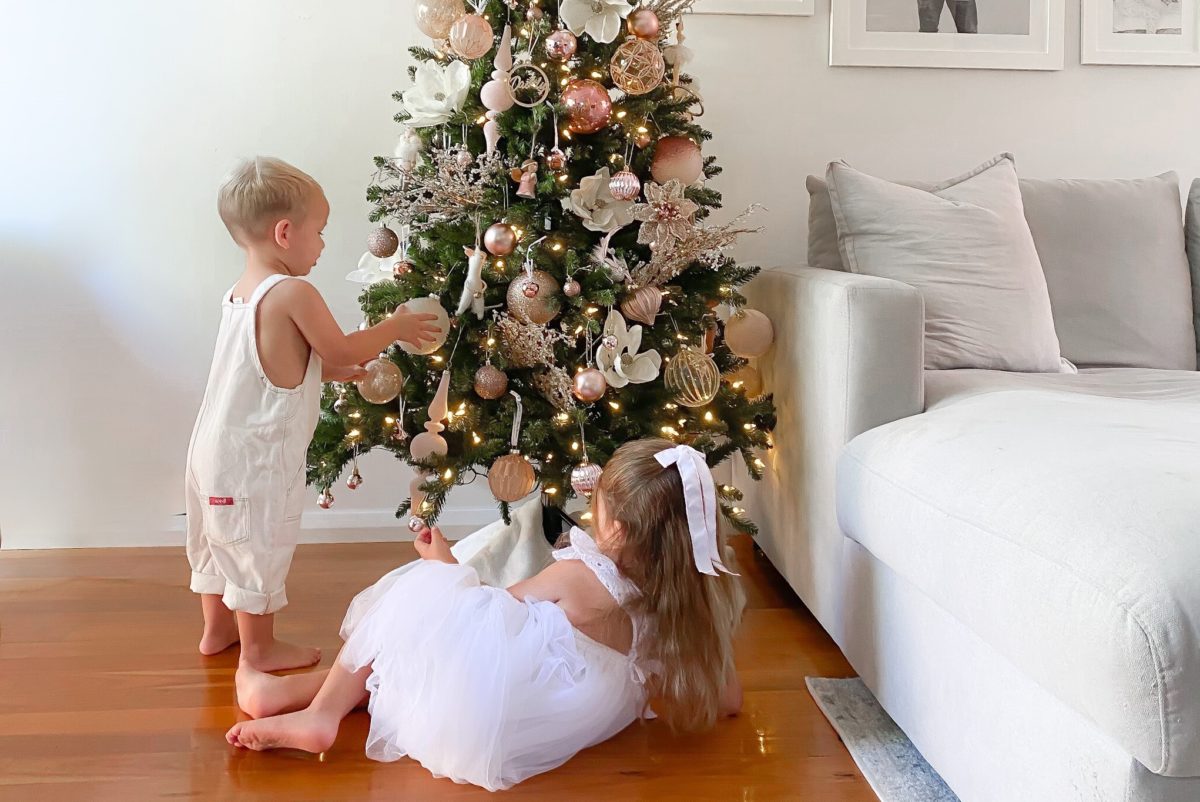 Two children playing with ornaments hung on a Balsam Hill Christmas tree