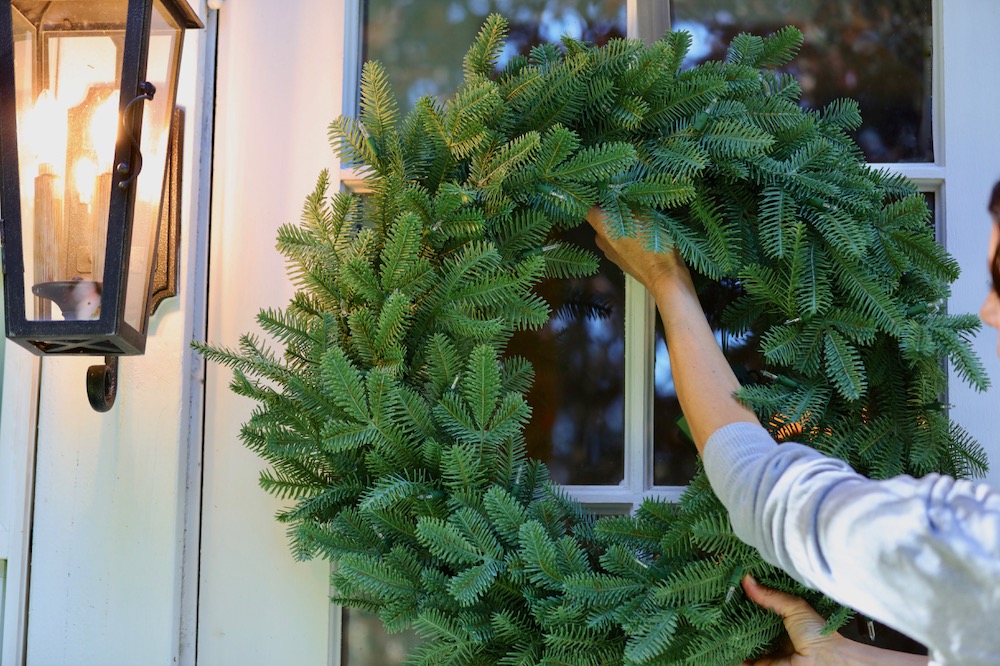 woman hanging an artificial wreath on a door