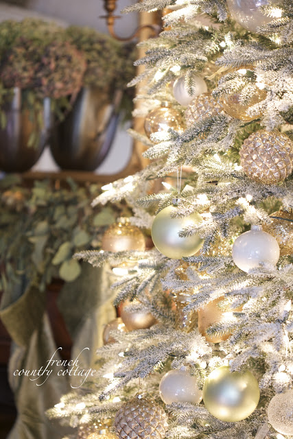 Closeup shot of a lit-up Christmas tree with frosted branches and assorted white and gold ornaments