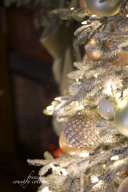 Closeup shot of a lit-up Christmas tree with frosted branches and assorted white and gold ornaments