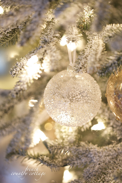 Closeup shot of a beaded globe-shaped ornament hanging from a lit-up Christmas tree