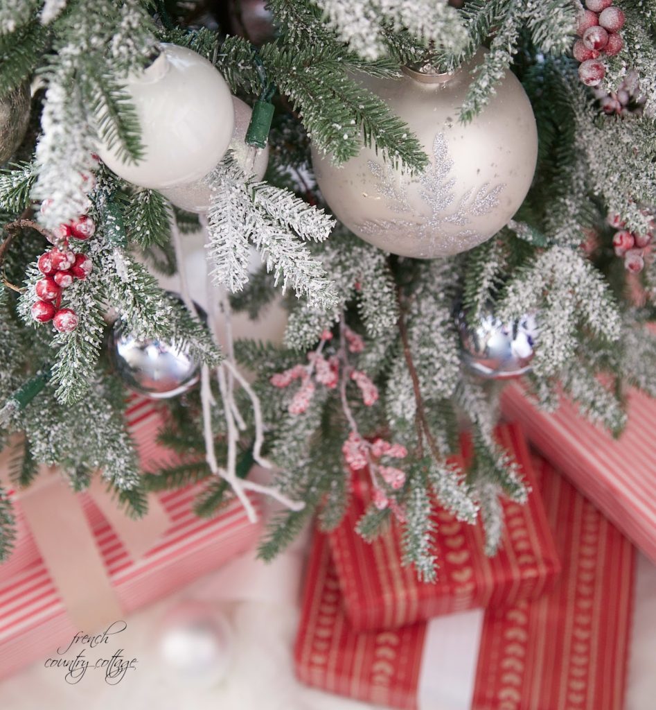 Champagne and white ornaments with frozen red berries and twigs on a frosted Christmas tree with gifts in red wrapping paper