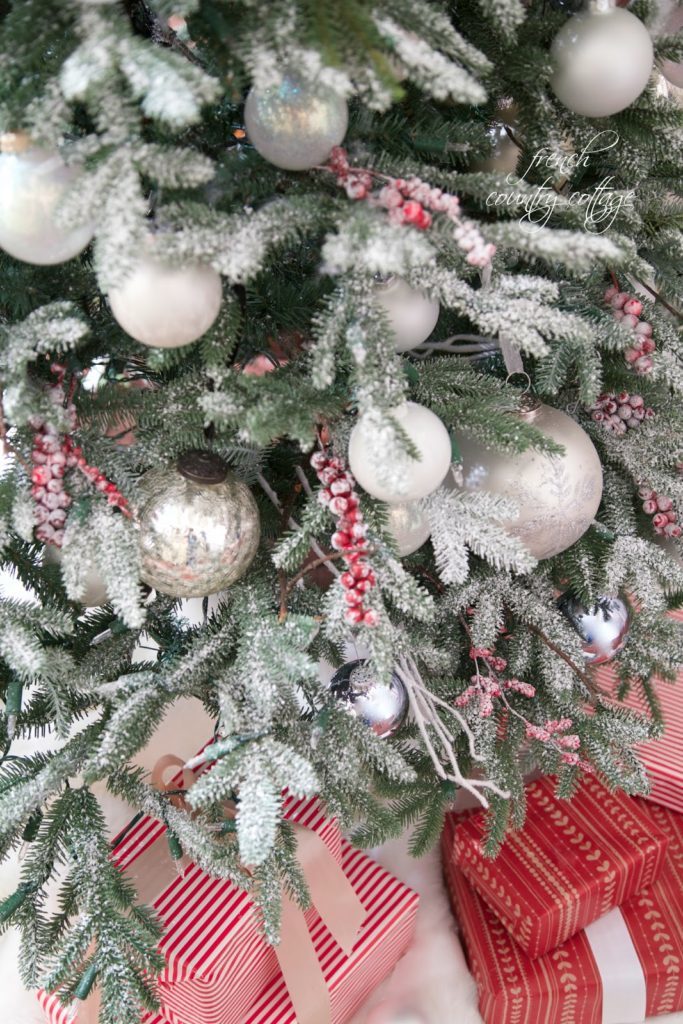 Downward shot of a simple rustic cottage Christmas tree decorated with white ornaments, frozen berries and twigs with gifts in candy cane striped wrapper