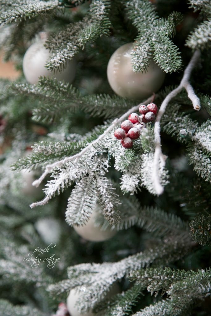 Frosted berries, twigs, and white ornaments on the branches of a simple rustic cottage Christmas tree