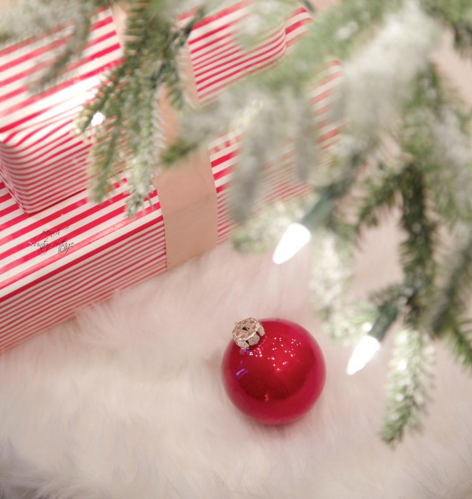 Red Christmas ornament on fur tree skirt with gifts wrapped in red and white striped wrappers