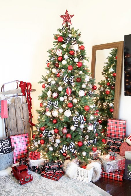 Christmas tree decorated with red, white, and black ornaments beside a mirror and a sled