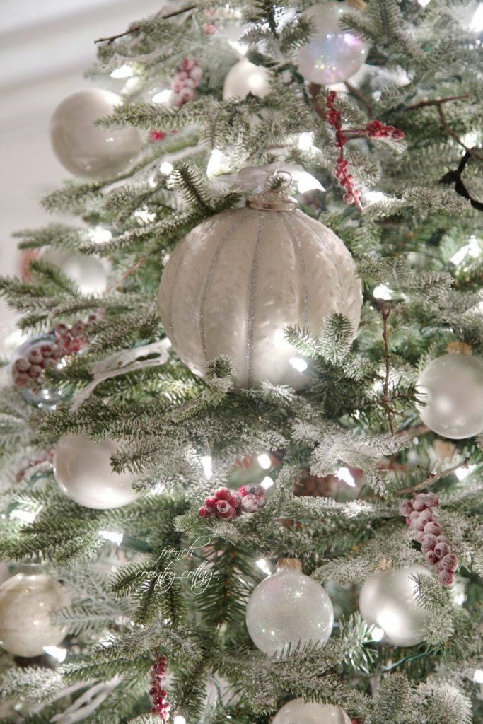 Closeup shot of white globe-shaped ornaments hanging from a lit-up Christmas tree.