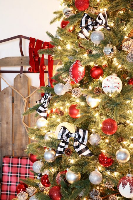 Pre-lit artificial Christmas tree decorated with red, white, and black ornaments beside a a sled