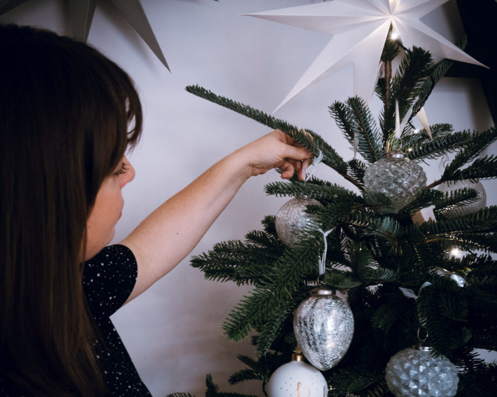 woman decorates christmas tree with glass ornaments