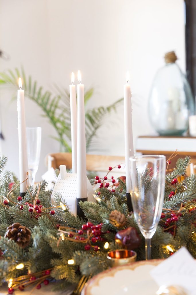 Closeup shot of a table setting with candlesticks, glasses, and artificial greenery