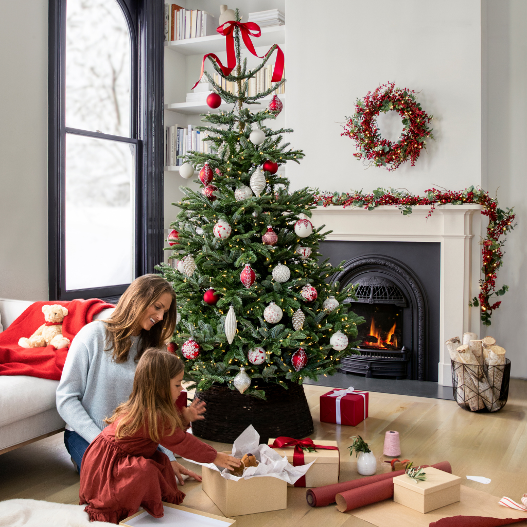 Mother and daughter wrapping gifts beside a Christmas tree