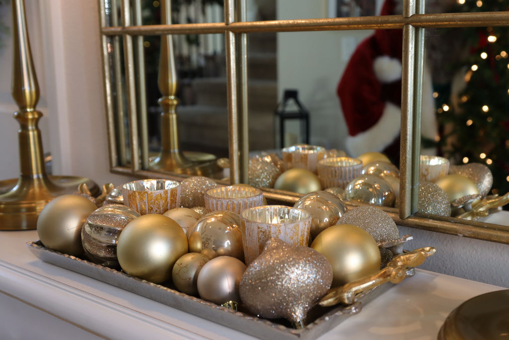 Gold Christmas ornaments and mercury glass votive holders on a tray on top of an entryway console