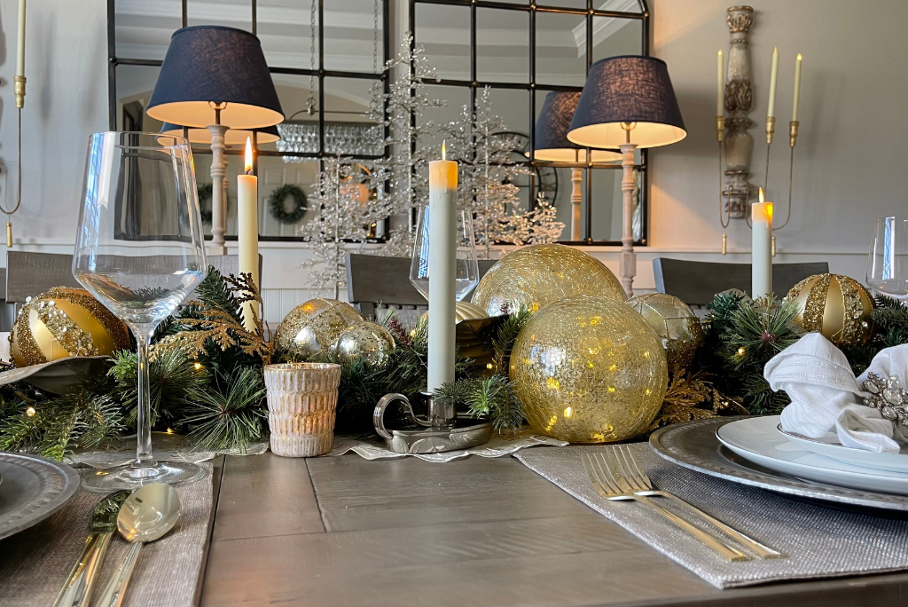 Christmas table centerpiece featuring decorated gold garland, glowing glass orbs, LED candles, votives, and mercury glass votive holders