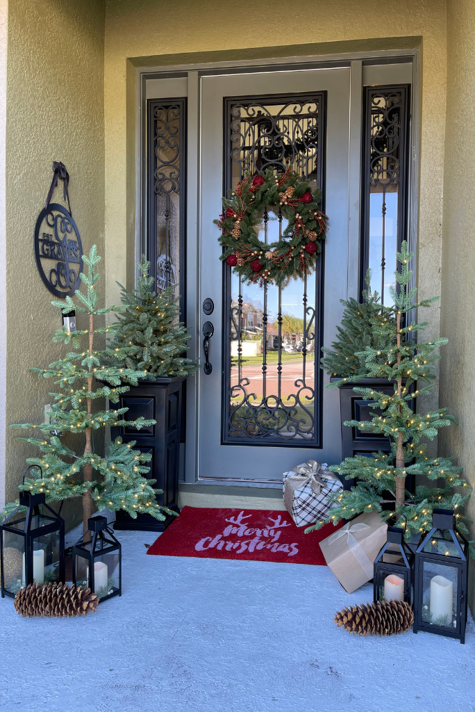 A Christmas wreath, small Christmas tree clusters, and LED lanterns as front door Christmas decor