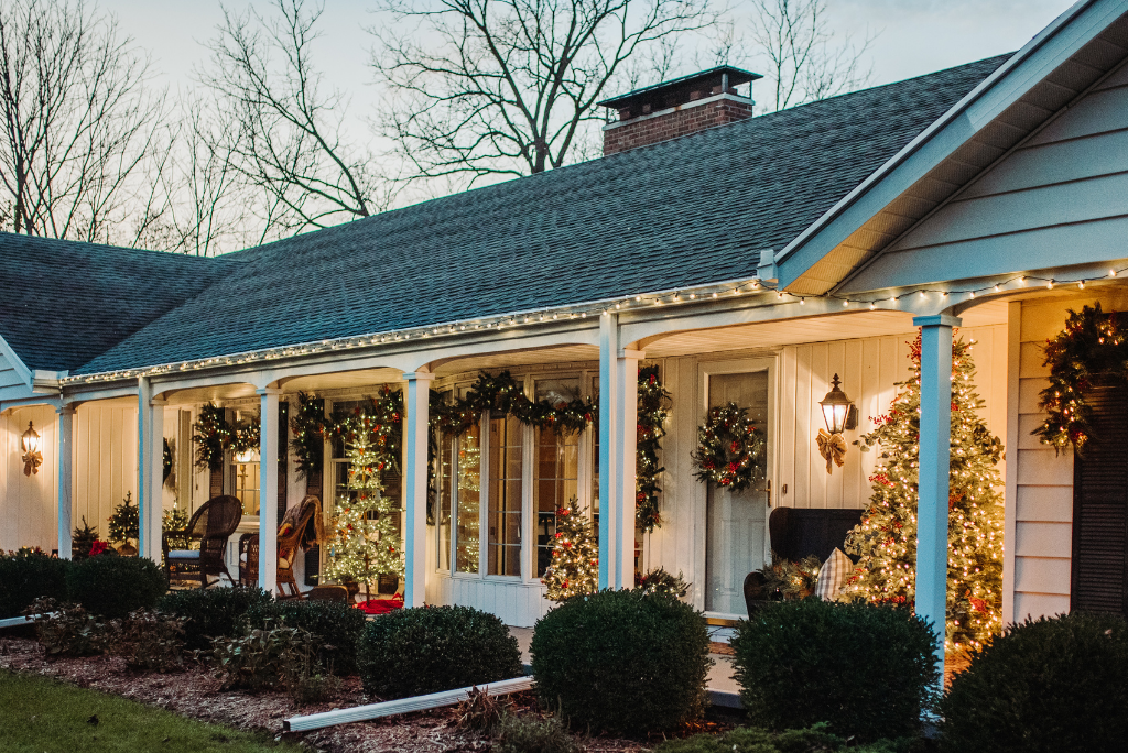 Front porch decorated with Christmas trees, garlands, and wreaths lit up at night