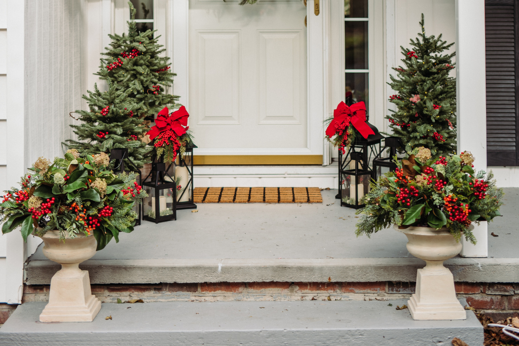 Small Christmas trees, lanterns, and potted foliage framing the front door entryway