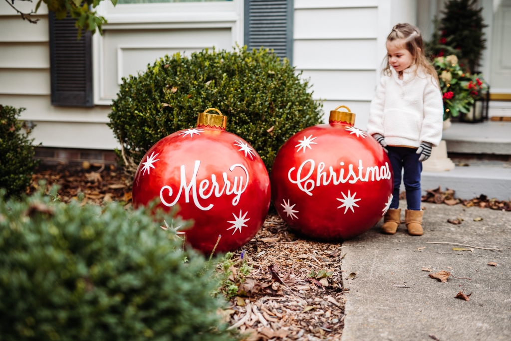 A little girl beside a pair of oversized outdoor Christmas ornaments in the front yard