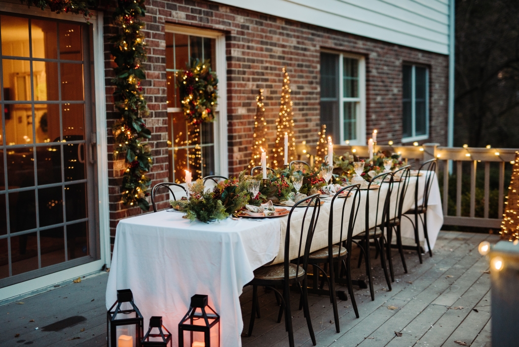 Outdoor patio decorated with a Christmas tablescape, lanterns, outdoor Christmas garlands, and wreath