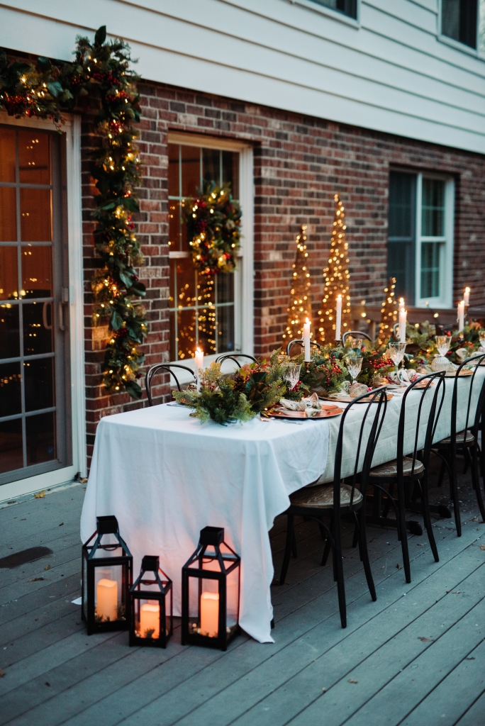 A long outdoor dining table on the patio at night decorated with pre-lit garlands and lanterns