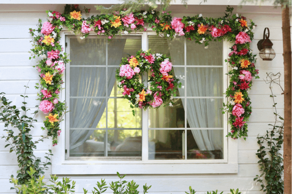 An exterior window decorated with an artificial floral wreath, garland, and window box 