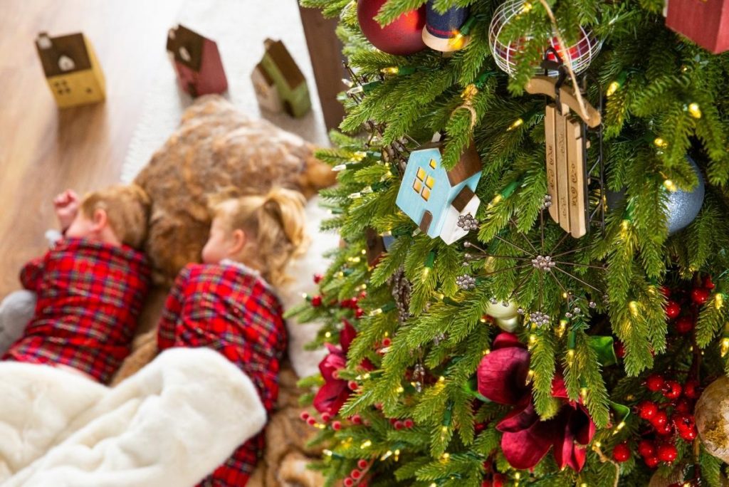 Two children sleeping on the floor beside a Christmas tree