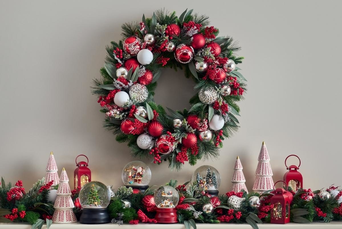 A Nordic style red and white Christmas wreath with snow globes, lanterns, and ceramic Christmas trees