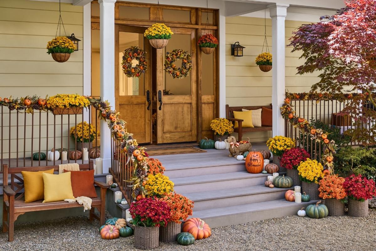 A front porch decorated with fall mums, pumpkins, and fall wreaths and garlands