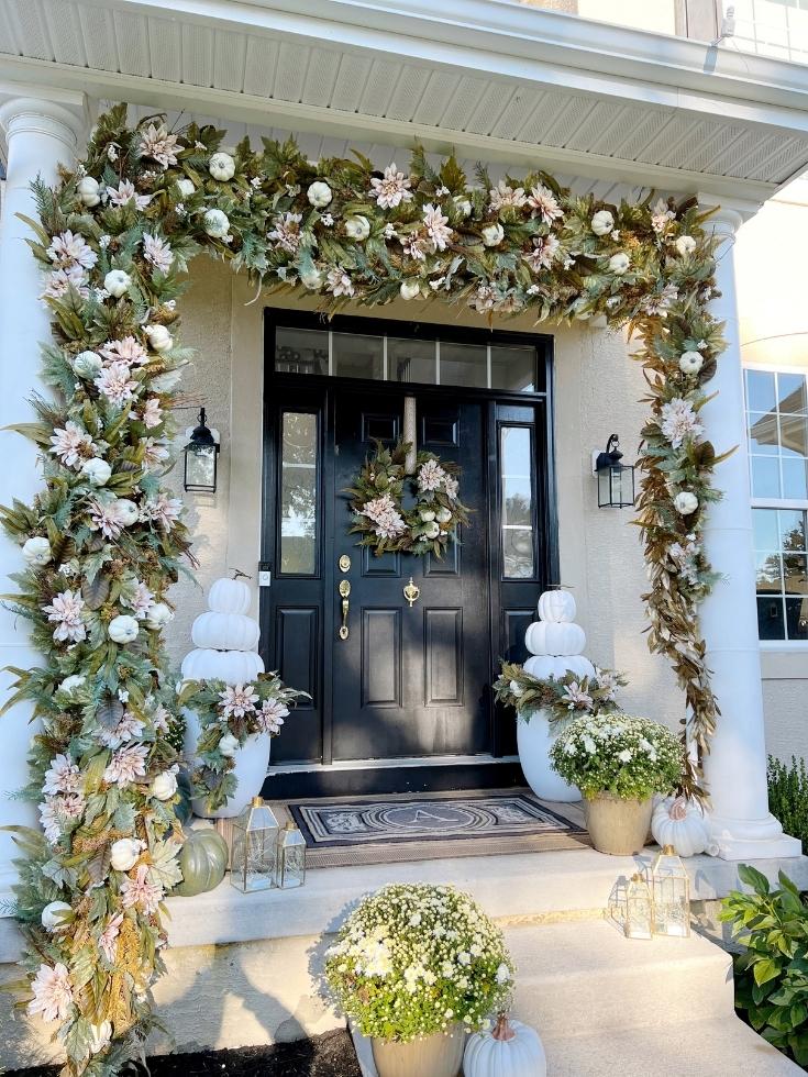 A front porch with a black door decorated with fall decor in a light fall color palette